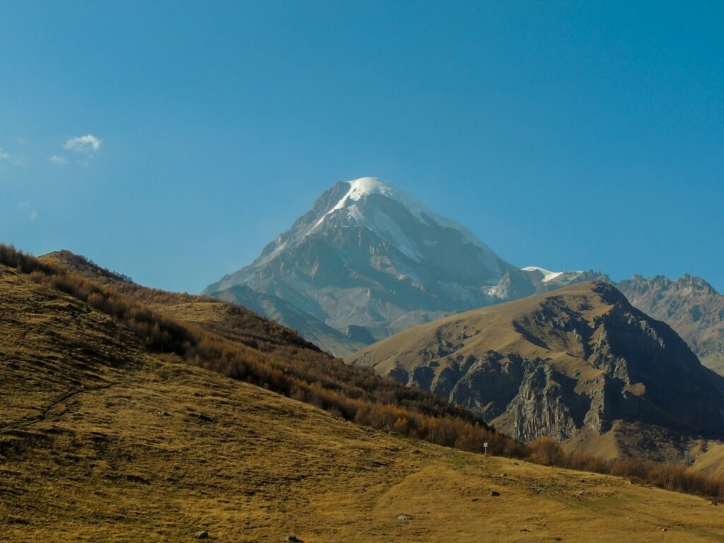 green grass field near snow covered mountain under blue sky during daytime
