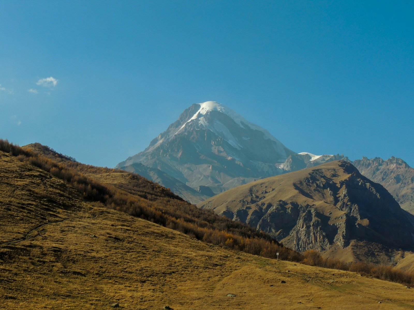 green grass field near snow covered mountain under blue sky during daytime